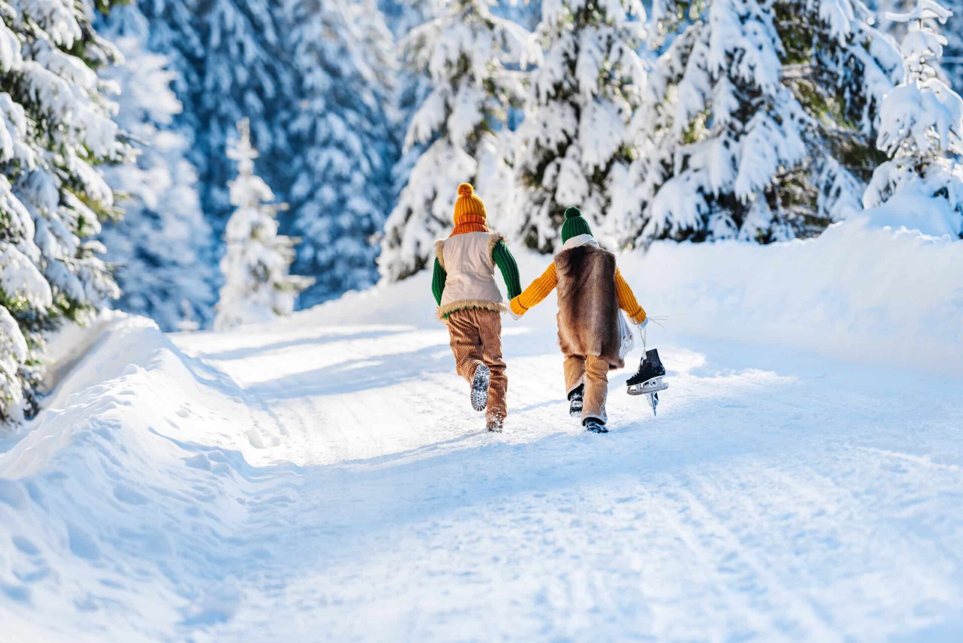 Winter family walk along a wonderful snowy forest road. Children run snow, back view. Sunny winter day.